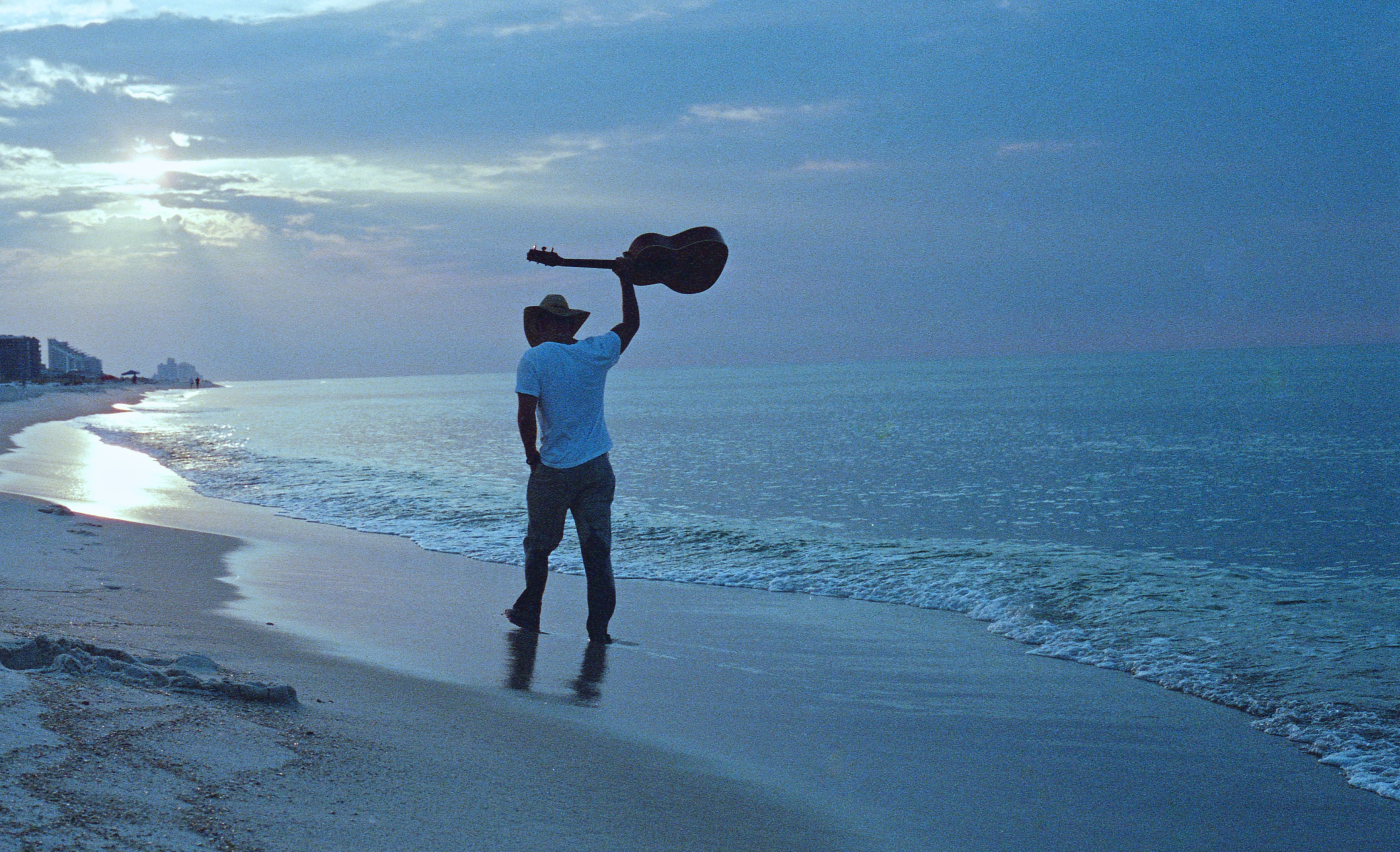 Kenny Chesney standing on a beach at sunrise with a guitar